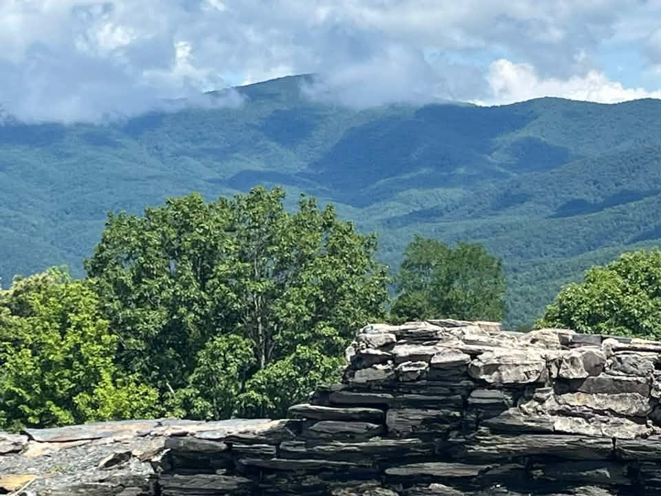 A view from Cohutta Overlook over layered blue-green ridges under drifting clouds, with a stacked stone wall in the foreground